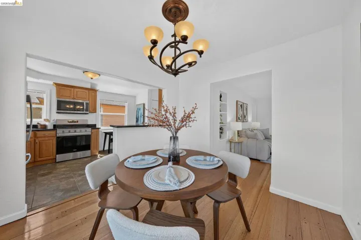 Dining area featuring wood-finish flooring, a decorative chandelier, and an open pass-through to the kitchen with wood cabinetry and stainless steel appliances
