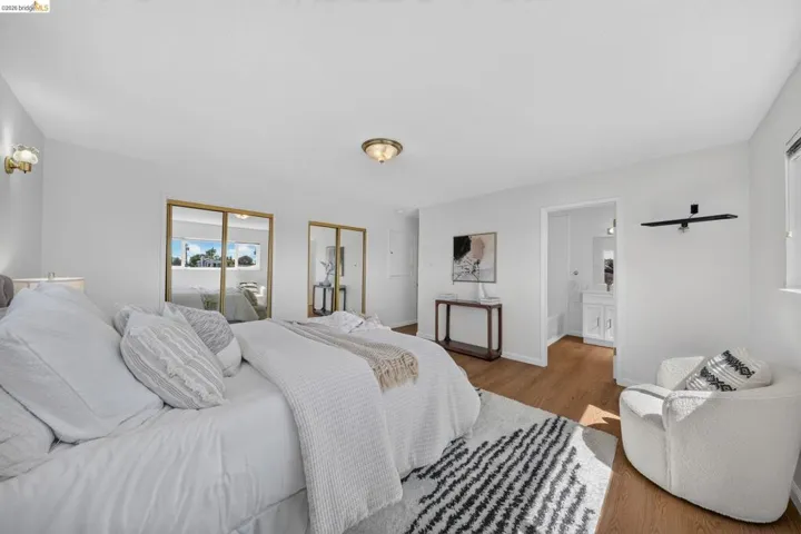 Bright bedroom featuring wood-finish flooring, white walls, and built-in mirrored closet doors