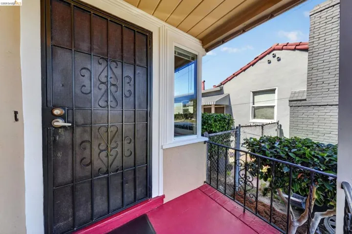 Wrought iron security door with decorative scrollwork, a covered porch with a red floor, and white trim