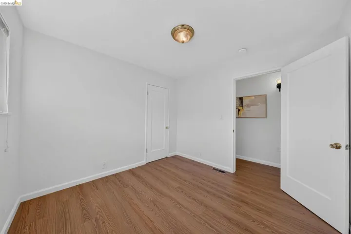 Bright room featuring wood-finish flooring, white baseboards, a single window, a flush mount ceiling light, and a white interior door