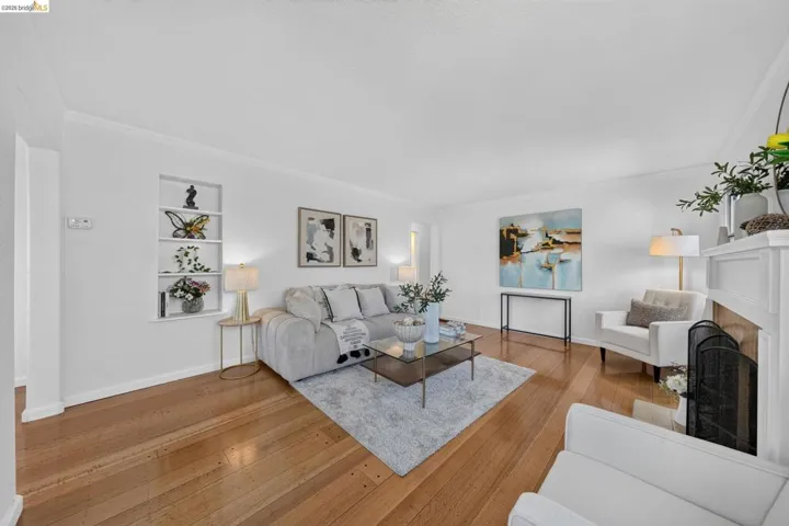 Living area featuring wood-finish flooring, a built-in display niche, a fireplace with a white mantel, and crown molding