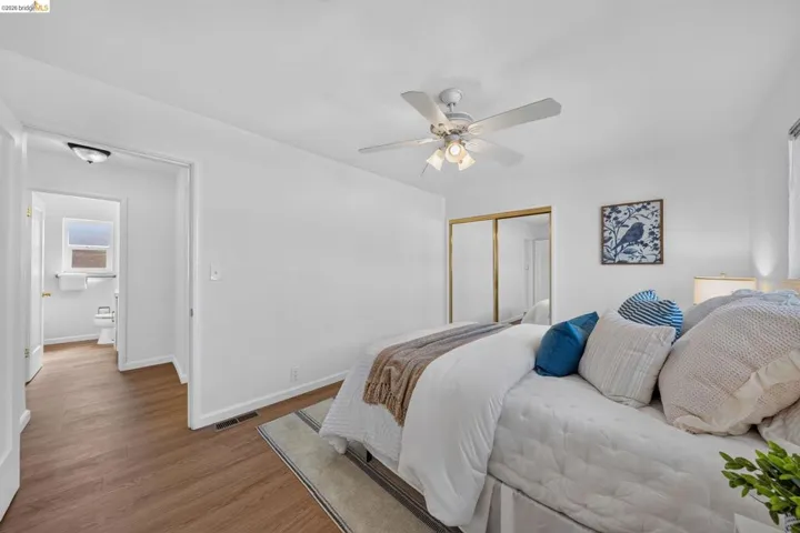 Bright room featuring wood-finish flooring, a ceiling fan with integrated lighting, and a mirrored closet with gold-tone framing