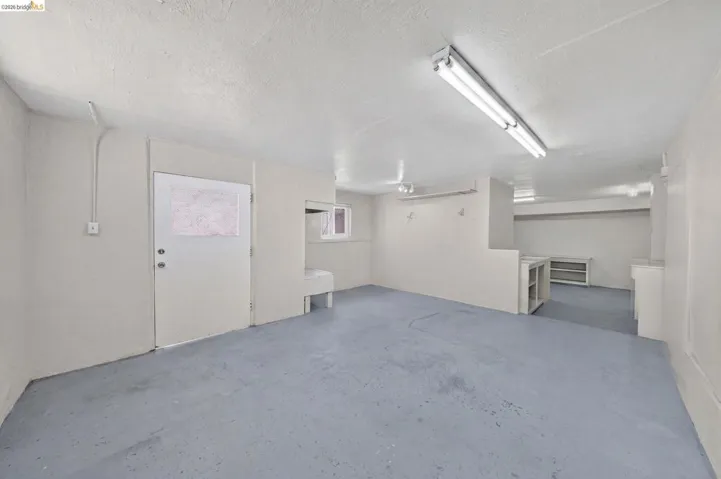 Spacious utility room featuring a painted concrete floor, white walls, overhead fluorescent lighting, and a window for natural light