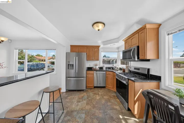 Kitchen featuring stainless steel appliances, light wood cabinetry, dark countertops, and multi-pane windows