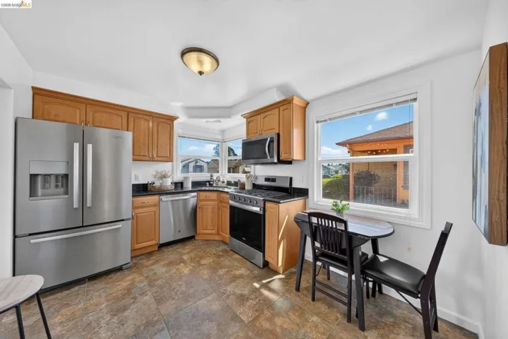 Kitchen featuring wood cabinetry, stainless steel appliances, dark countertops, and tile flooring