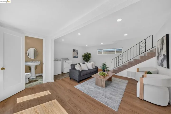 Open concept living area with wood-finish flooring, recessed lighting, and a carpeted staircase featuring an ornate metal railing
