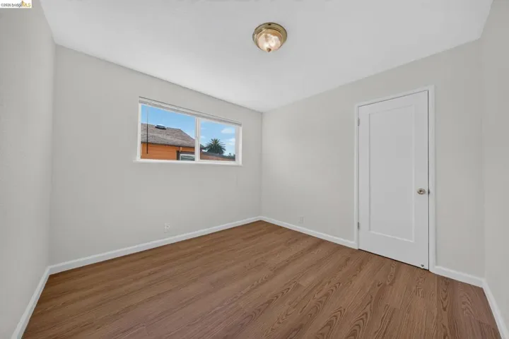 Bright room featuring wood-finish flooring, light gray walls, white baseboards, a white paneled door, and a multi-pane window