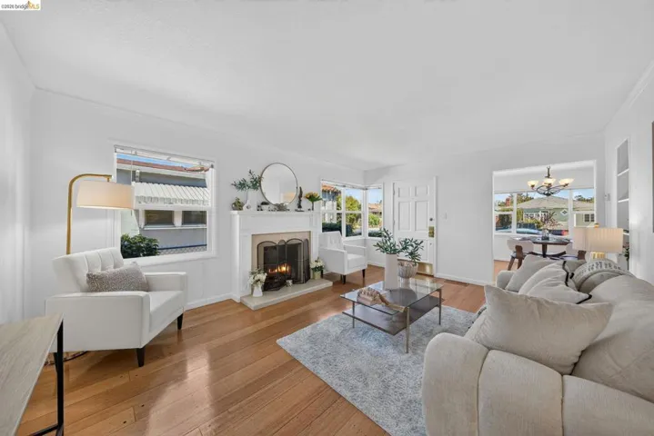 Living room featuring hardwood flooring, a white mantel fireplace, multiple windows, and a white paneled entry door