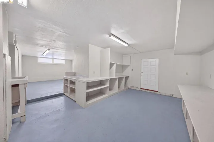 Spacious utility area featuring light blue flooring, white walls, built-in shelving, a full-lite door, and a utility sink