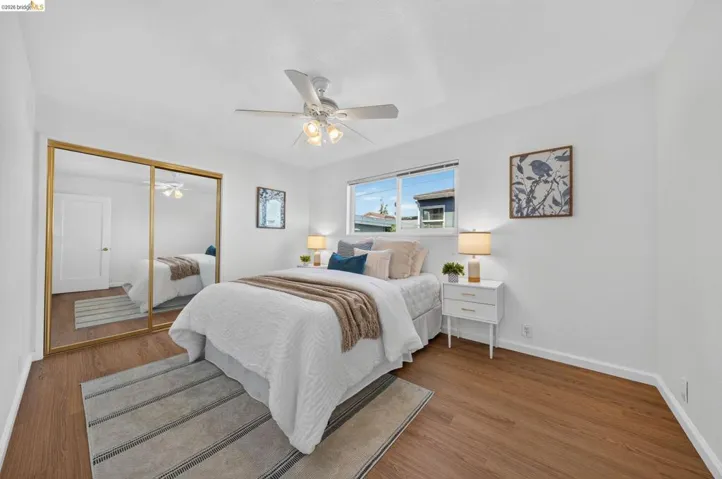 Bedroom featuring wood-finish flooring, a ceiling fan, and a large window providing ambient light