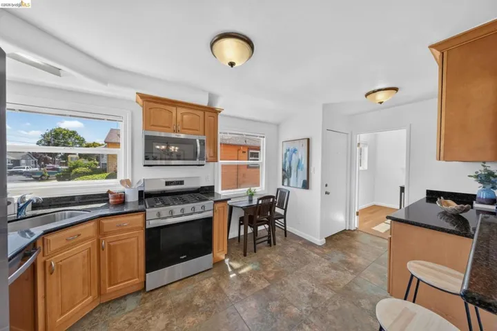 Kitchen featuring wood cabinetry, stainless steel appliances, dark stone countertops, and tile flooring