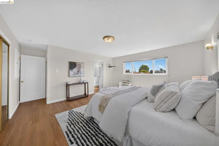 Spacious room featuring wood-finish flooring, light neutral wall tones, a large window offering natural illumination, and a ceiling-mounted light fixture