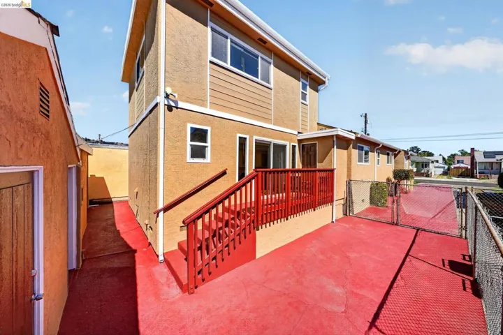 Rear exterior featuring a two-story structure with stucco and horizontal siding, a red-painted deck, and a red-painted concrete patio