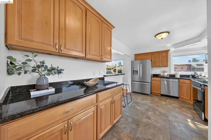 Kitchen featuring wood cabinetry, dark granite countertops, stainless steel appliances, and a tiled floor