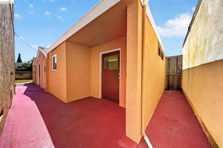 Exterior access pathway featuring a covered entry, stucco siding, and a red-painted concrete surface