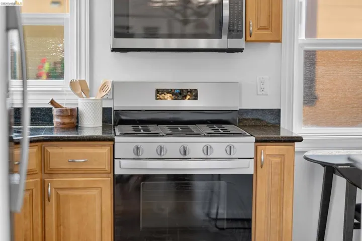 Stainless steel range with an overhead microwave, granite countertops, and light wood cabinetry