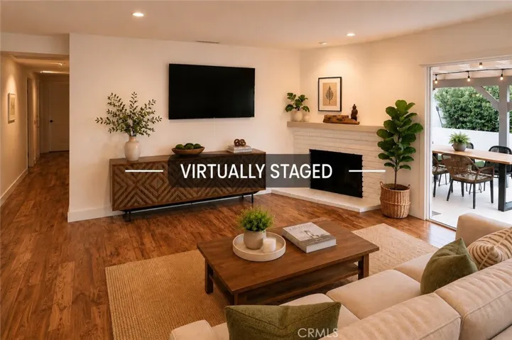 Gather in the inviting living room featuring a charming corner fireplace, spacious media wall, and sliding glass doors that create a seamless connection to the covered patio and beautifully landscaped backyard. (Virtually staged.)