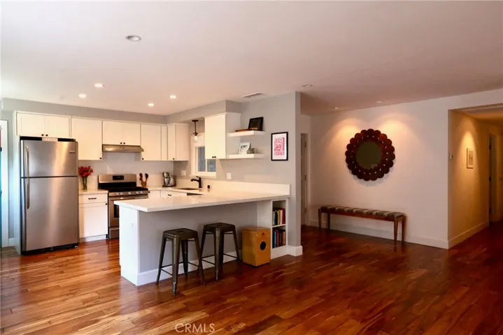 The open-concept kitchen features crisp white cabinetry, quartz countertops, stainless steel appliances, a spacious center island with bar seating, and convenient built-in shelving—perfect for everyday living and entertaining.