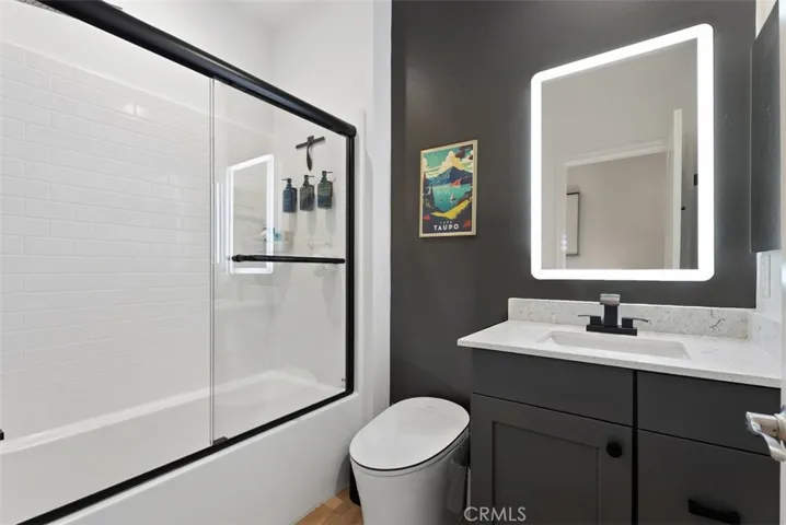 The beautifully upgraded secondary bathroom showcases a rain shower head, upgraded glass shower enclosure, Toto bidet toilet, designer LED mirror lighting, and newly installed luxury vinyl plank flooring for a modern spa-inspired feel.