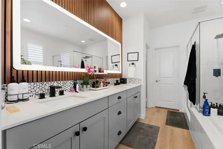 The spa-inspired primary bath features dual vanities, quartz countertops, new designer LED lighted mirror and matte black fixtures, designer tile backsplash, a custom wood slat accent wall, and abundant storage.