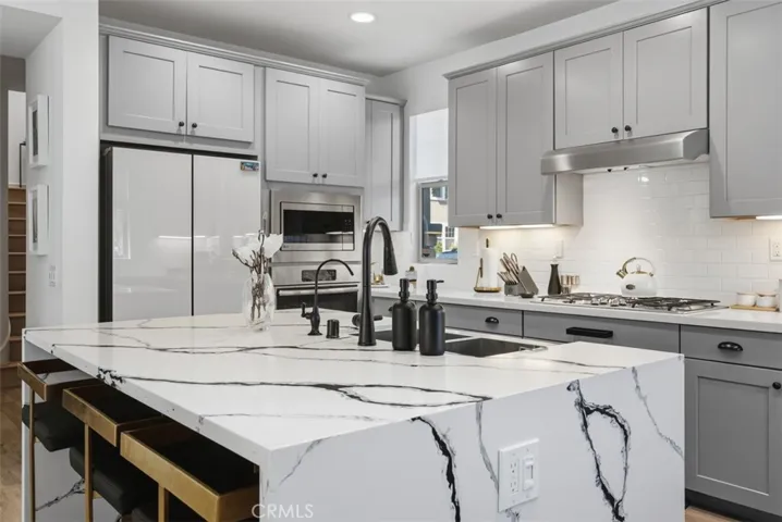 The showstopping marble island offers generous seating and prep space, complemented by a matte black pull-down faucet, stainless steel undermount sink, and designer finishes throughout. The ceiling above the island is prewired for three designer pendant lights to complete the space.
