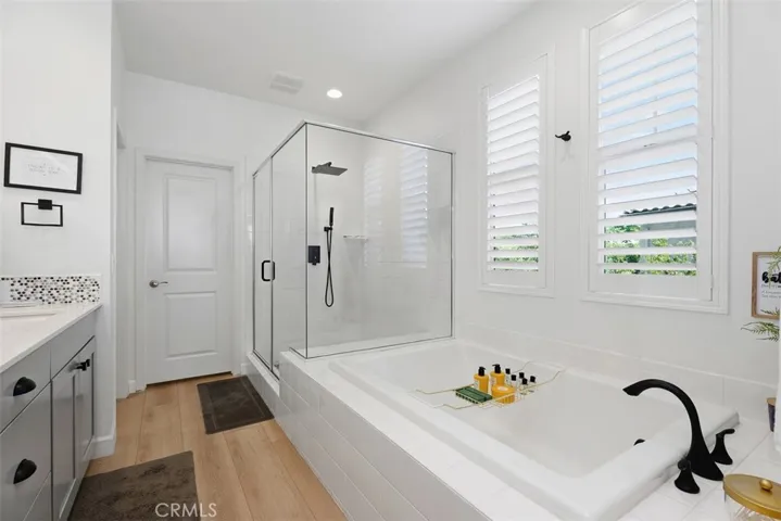 The spa-inspired primary bath showcases a new glass shower enclosure, matte black fixtures, a luxurious rain shower head, soaking tub, and plantation shutters that fill the space with natural light.
