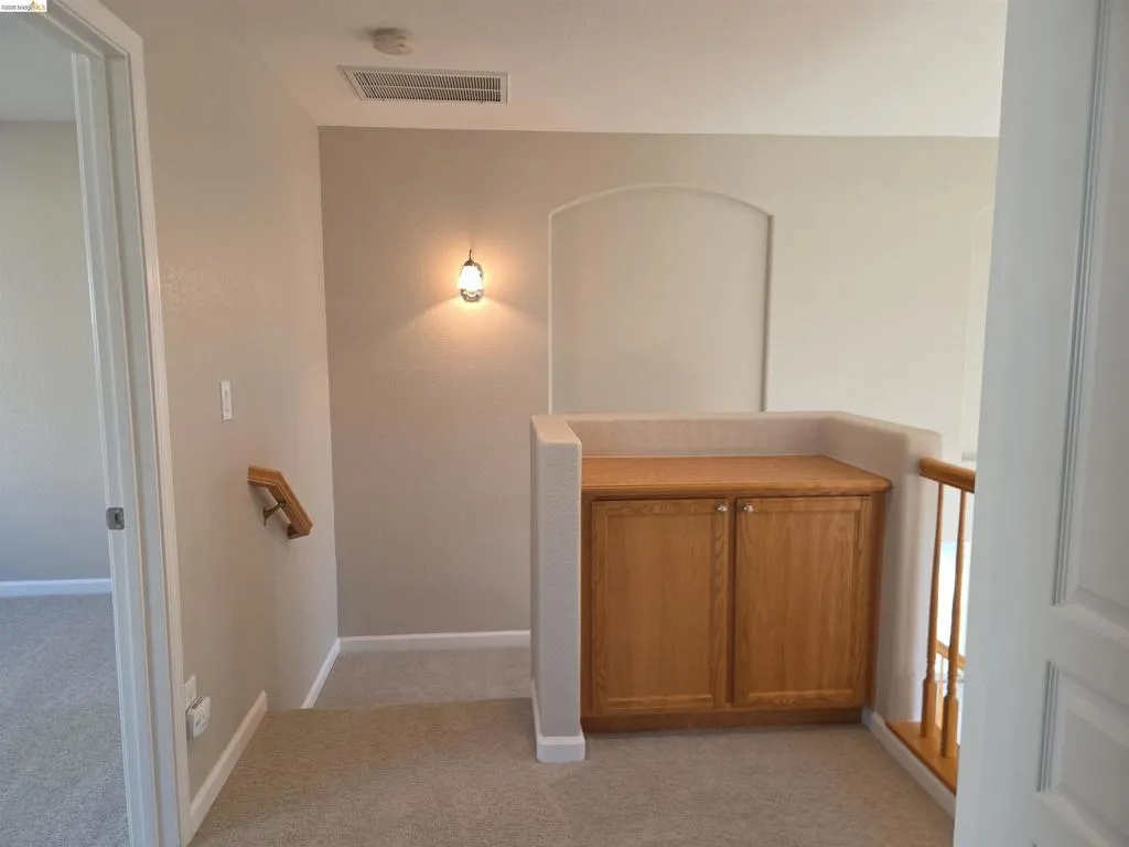 Upper-level landing featuring a built-in wood-finish cabinet with hardware, an arched wall niche, and a wall-mounted sconce