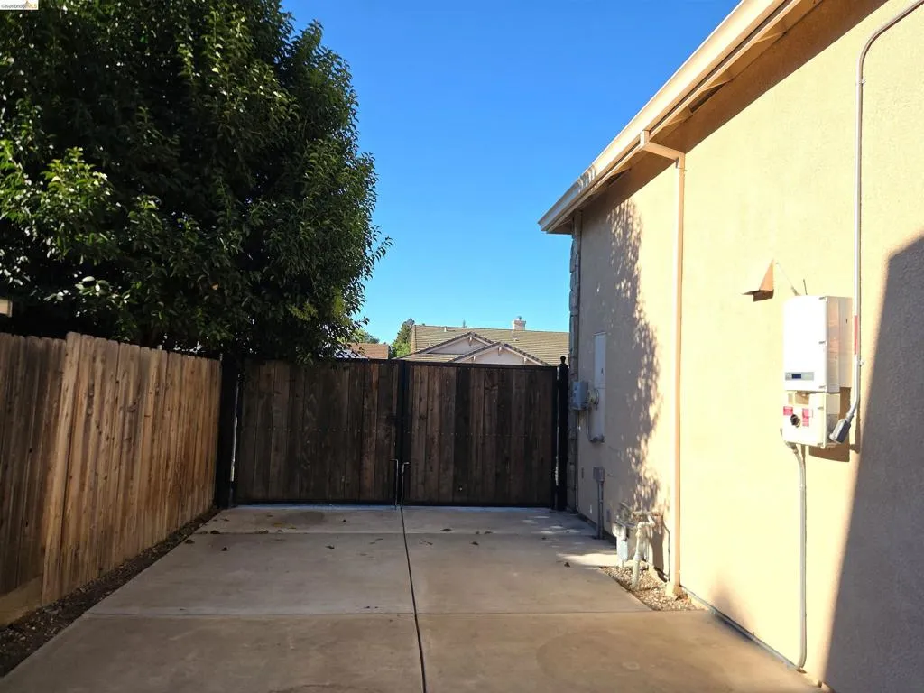 Paved side yard featuring a privacy fence, secure gate, stucco siding, and a tankless water heater