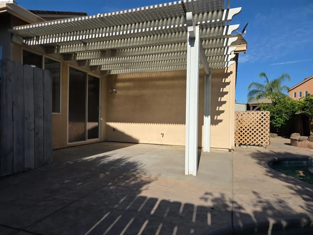 Patio featuring a white slatted pergola, sliding glass door entry, concrete flooring, and a partial view of a pool