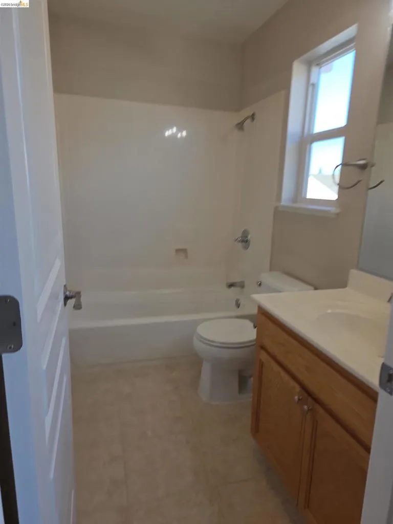 Bathroom featuring a tub and shower combination with chrome fixtures, a single-pane window, a wood-finish vanity with a built-in sink, and light-toned tile flooring