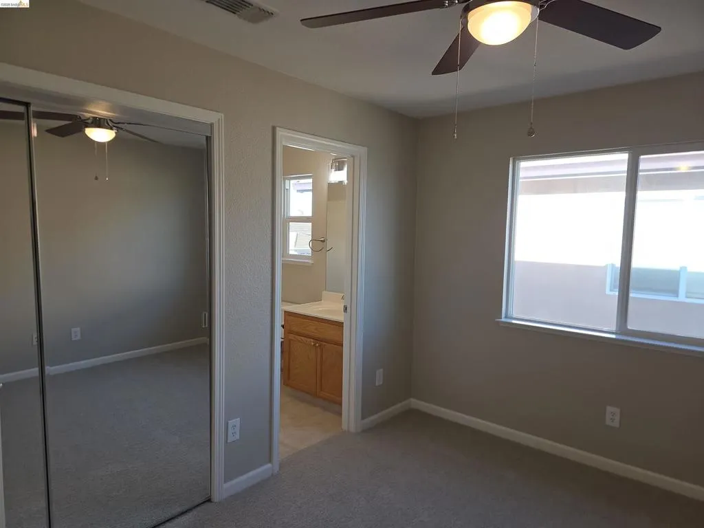 Carpeted room featuring a ceiling fan with integrated lighting, mirrored sliding closet doors, and a window with white framing