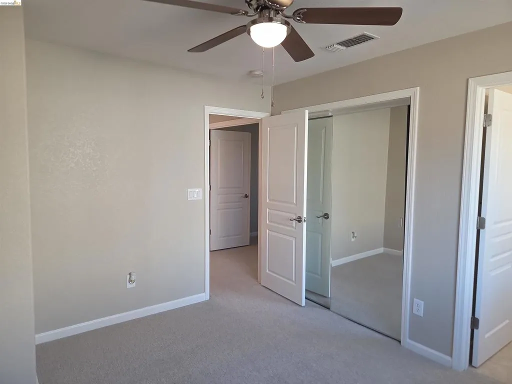 Carpeted room featuring a ceiling fan with integrated lighting, mirrored sliding closet doors, and neutral wall paint