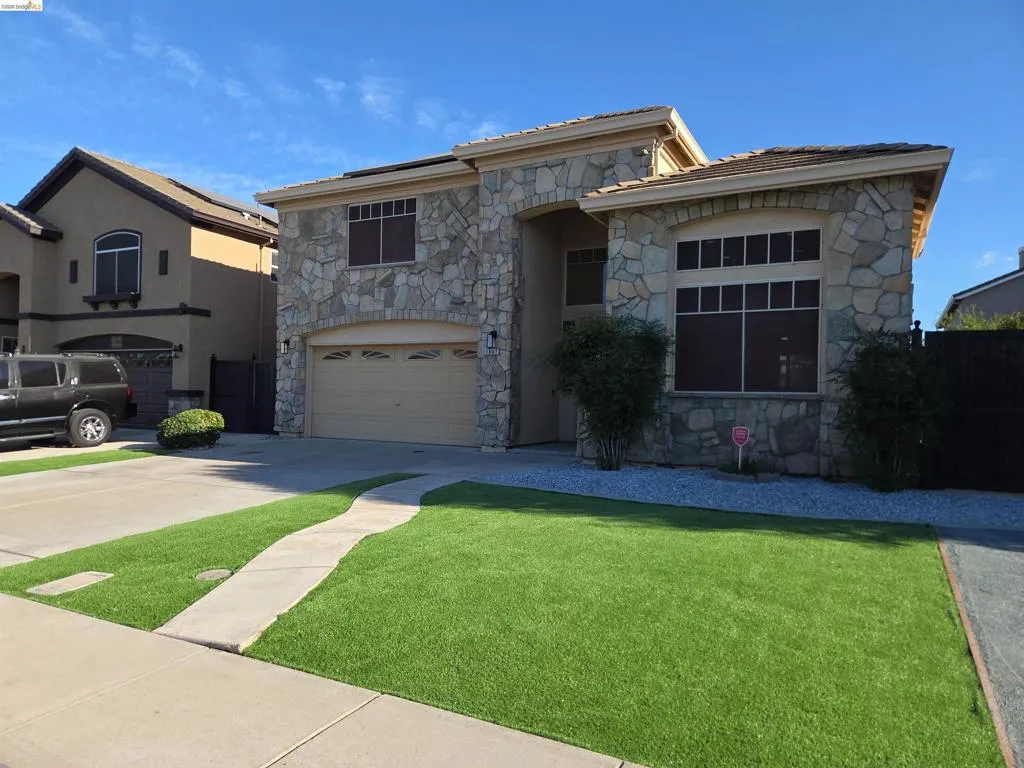 Stone facade residence featuring a two-car garage, partial stucco exterior, and solar panels