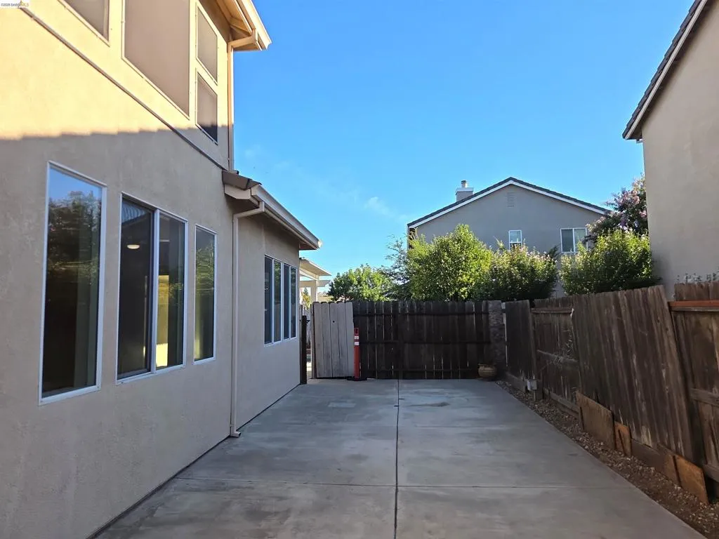 Concrete side yard featuring stucco exterior, multiple windows, and a wood fence