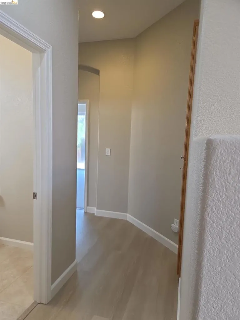 Hallway with light wood-finish flooring, recessed lighting, neutral paint, white trim, and an arched doorway