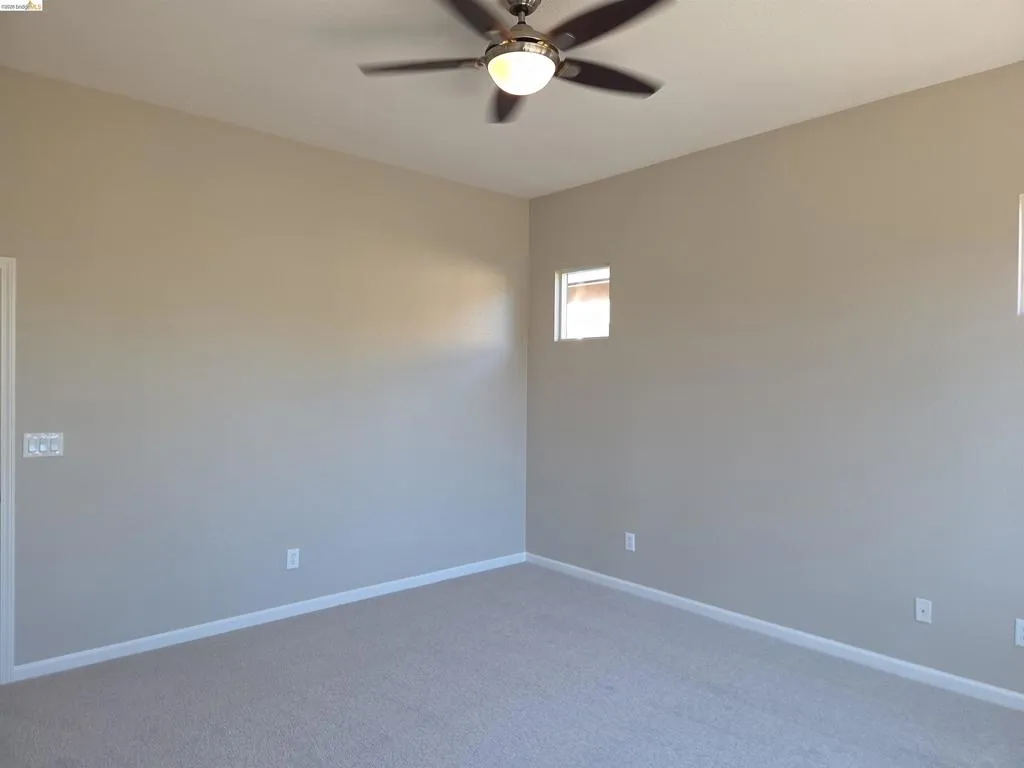 Carpeted interior space featuring a ceiling fan with integrated lighting, a high window, and neutral wall tones