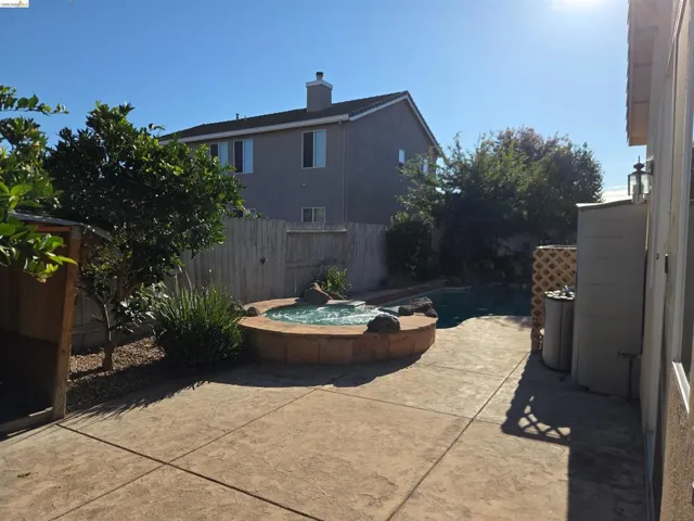 Backyard featuring a built-in hot tub, concrete patio, and mature landscaping