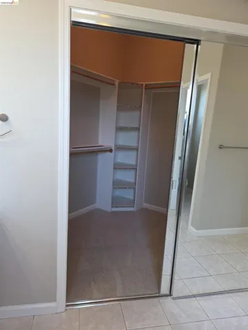 Walk-in closet with mirrored sliding doors, built-in shelving, hanging rods, and carpet flooring