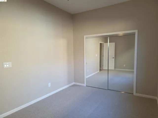 Spacious room featuring neutral wall paint, light-colored carpet flooring, white baseboards, and a large mirrored closet door