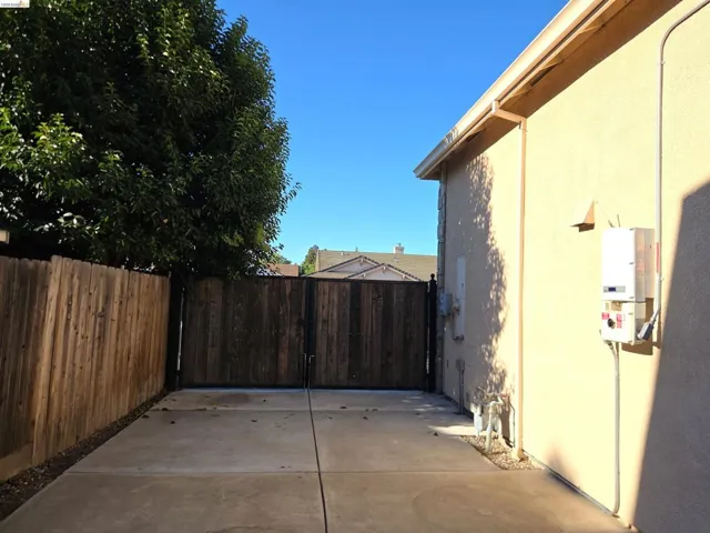 Paved side yard featuring a privacy fence, secure gate, stucco siding, and a tankless water heater