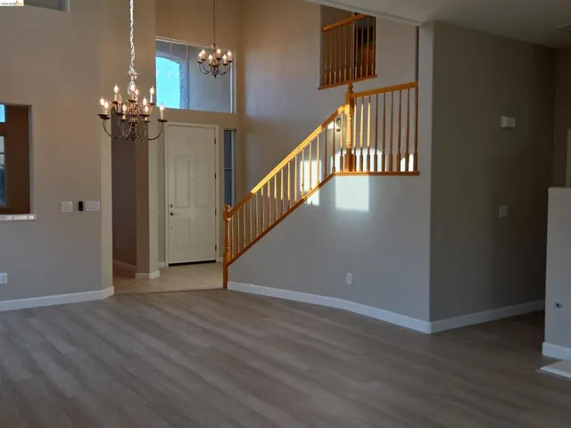 Spacious entry foyer featuring a light wood-finish flooring, a grand staircase with wood railings, a multi-paneled entry door, and a decorative chandelier