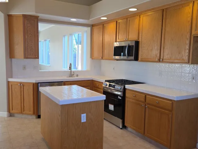 Kitchen featuring wood cabinetry, white tile countertops, a stainless steel gas range, a built-in microwave, and an undermount sink