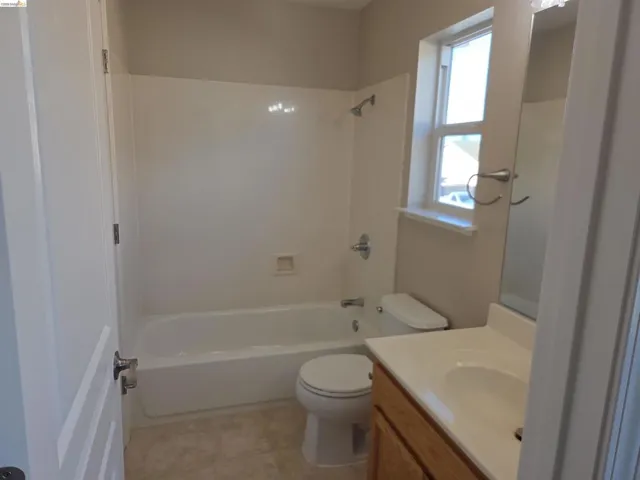 Full bathroom featuring a white tub/shower combination, toilet, and vanity with an integrated sink