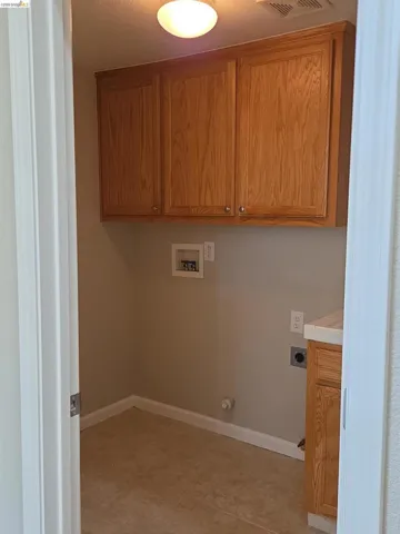 Laundry area featuring overhead wood-finish cabinetry, a built-in counter with a matching wood-finish base cabinet, tile flooring, and utility hookups
