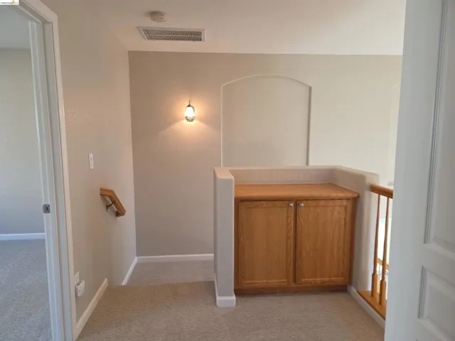 Upper-level landing featuring a built-in wood-finish cabinet with hardware, an arched wall niche, and a wall-mounted sconce