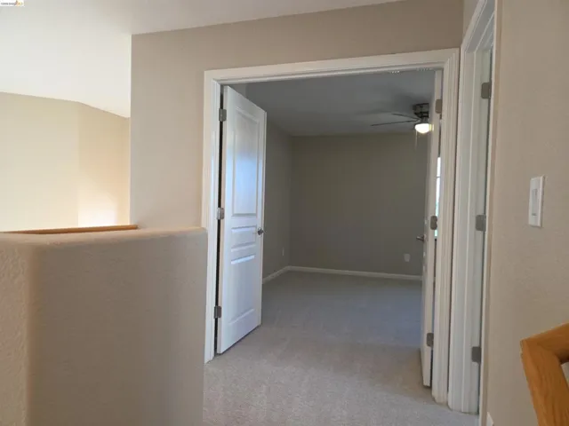 Carpeted interior space featuring a double-door entry, neutral wall color, and a ceiling fan with integrated lighting