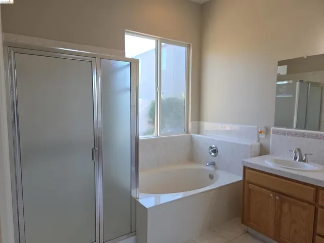 Bathroom featuring a corner soaking tub with tile surround, a separate shower with frosted glass doors, a single vanity with wood cabinetry, and an integrated sink with a light-colored countertop