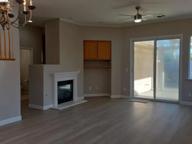 Living area featuring wood-finish flooring, a fireplace with a white mantel, built-in wooden cabinetry, a ceiling fan with integrated lighting, and a sliding glass door to the exterior