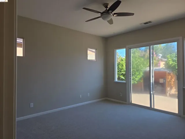 Spacious room featuring neutral carpeting, a modern ceiling fan, and a large sliding glass door with an adjacent window providing outdoor access