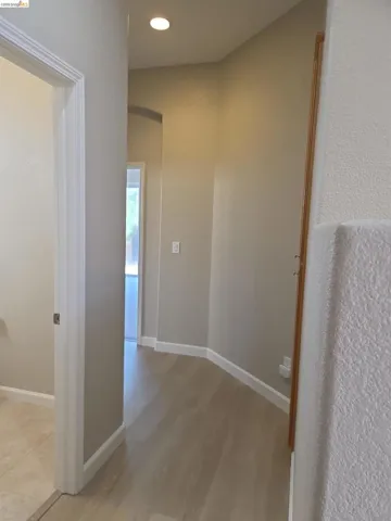 Hallway with light wood-finish flooring, recessed lighting, neutral paint, white trim, and an arched doorway